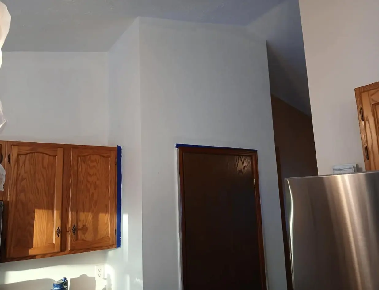 Modern kitchen with white walls, wooden cabinets, a dark brown door, stainless steel refrigerator, and blue painter's tape for a fresh home renovation.