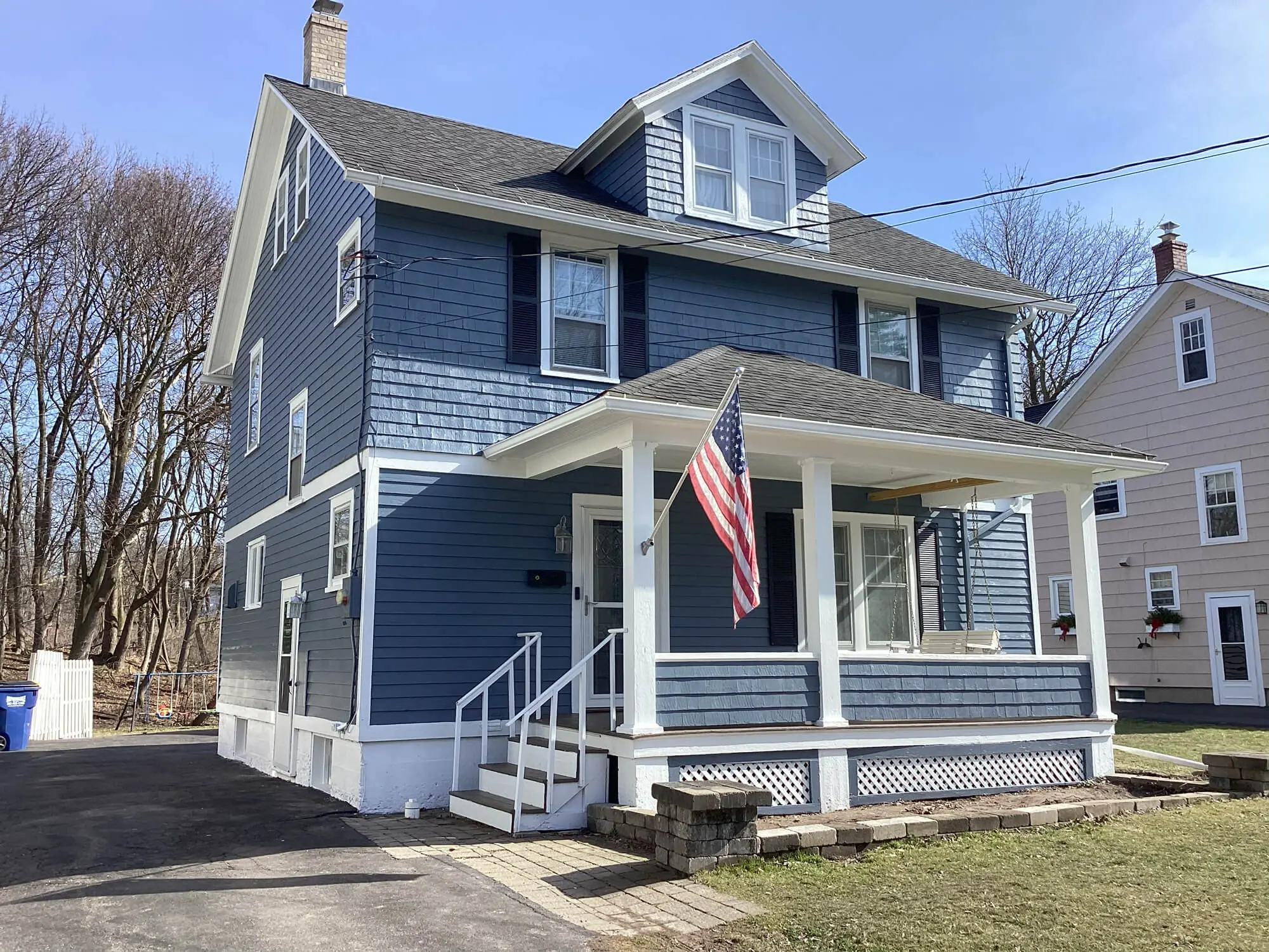 A charming blue two-story house with a white porch and American flag, surrounded by trees, ideal for real estate and home decor SEO.