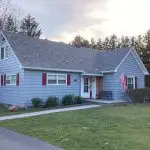 A house with a white porch and American flag, surrounded by trees, ideal for real estate and home decor