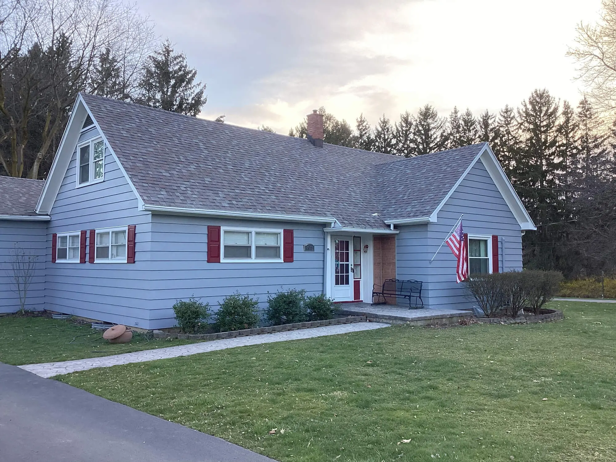 A house with a white porch and American flag, surrounded by trees, ideal for real estate and home decor