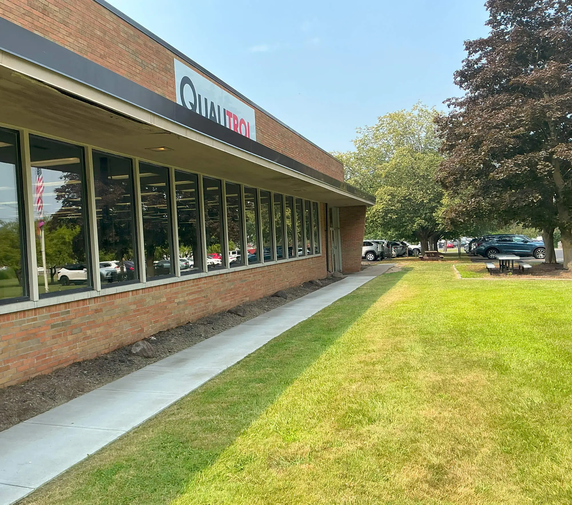 Qualtrics office building with a modern brick facade, large windows, and a well-maintained lawn, featuring a sign with the company logo, surrounded by trees and parked cars