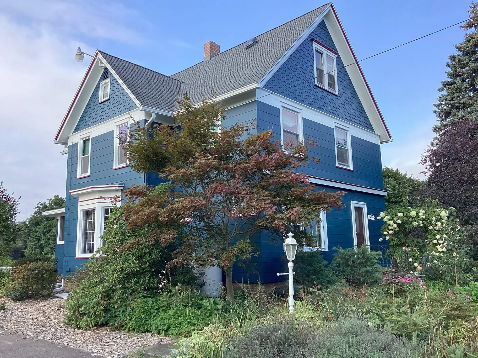 Modern beach house with large glass windows, wooden deck, and ocean view under a sunny afternoon sky.