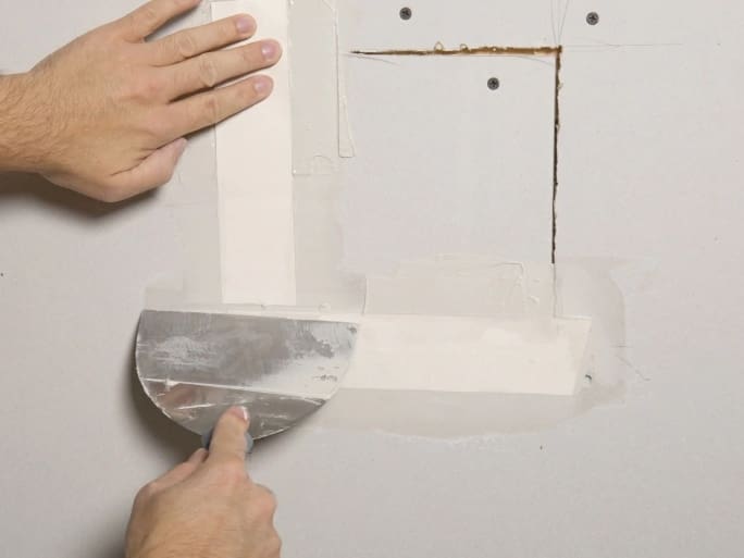 A person applying drywall joint compound with a putty knife to repair a wall seam, enhancing home improvement and construction SEO.