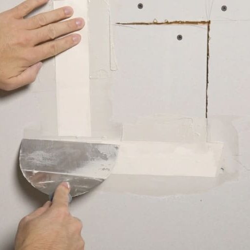 A person applying drywall joint compound with a putty knife to repair a wall seam, enhancing home improvement and construction SEO.